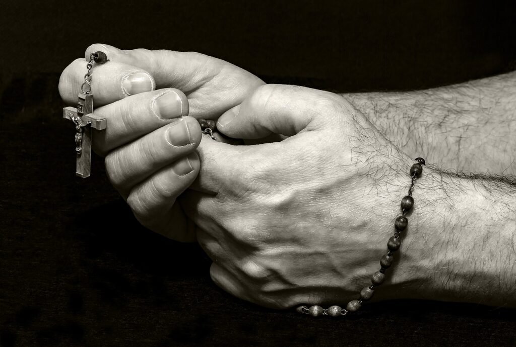 Mains tenant un chapelet noir avec une croix chrétienne, symbole de prière et la force de surmonter chaque épreuve.