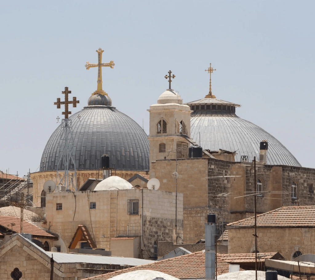 Vue sur les dômes de l'Église du Saint-Sépulcre à Jérusalem, avec des croix chrétiennes ornant les sommets des coupoles, sous un ciel dégagé. Référence au dialogue islamo-chrétien